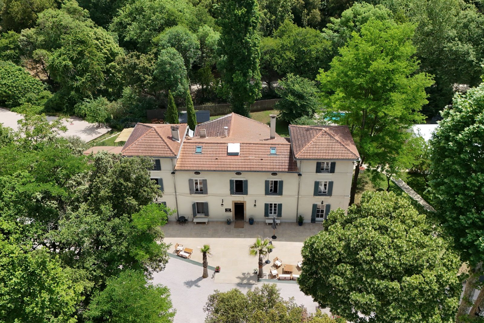 Vue aérienne d'une bastide entourée d'arbres, avec sa cour et sa piscine