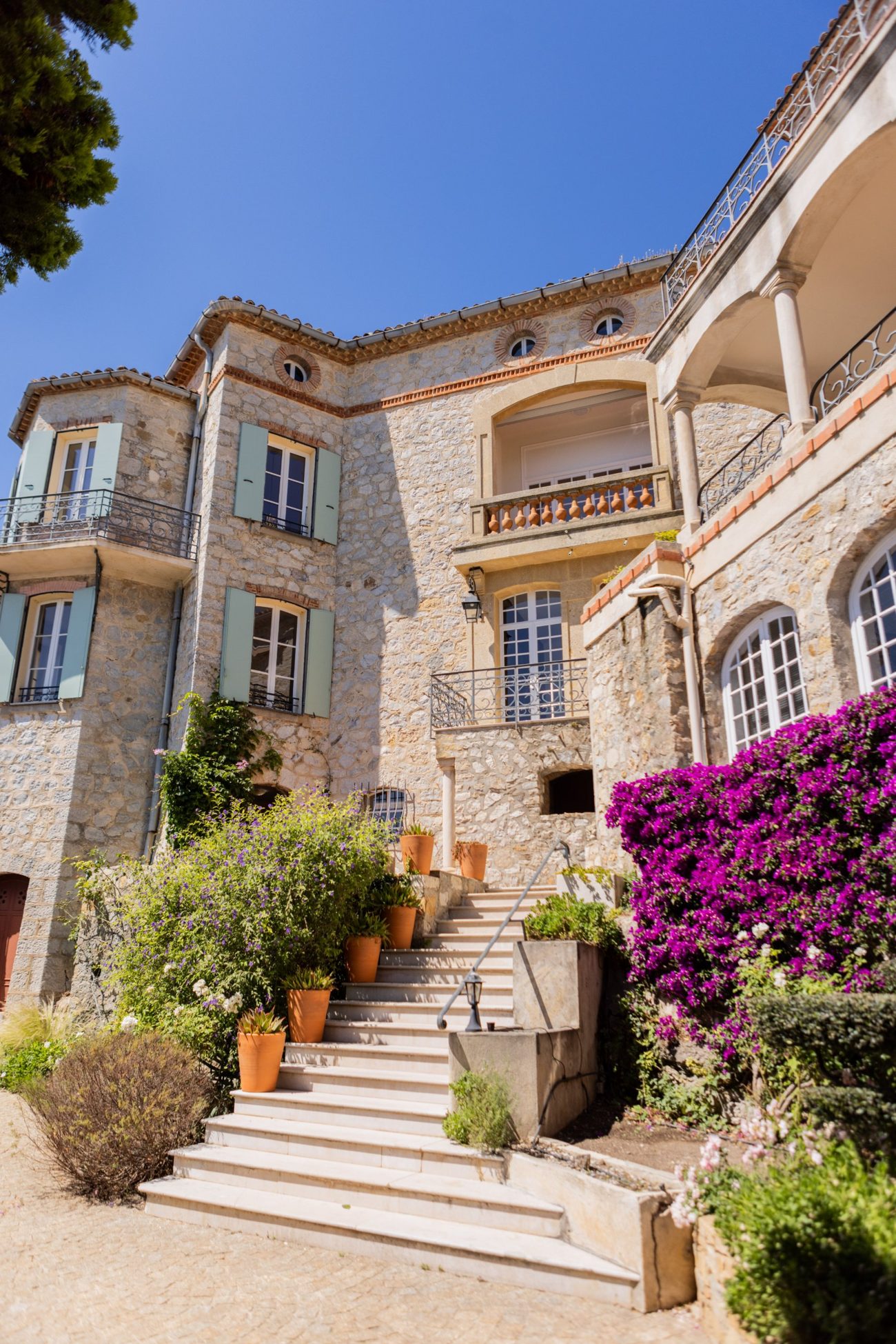 Façade en pierre du Château des Costes, escalier fleuri et bougainvillier