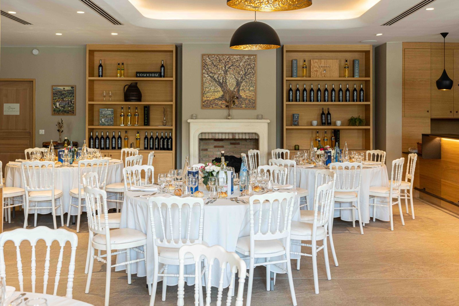 Salle de réception du Domaine Souviou dressée pour un déjeuner d'entreprise, tables rondes et cheminée